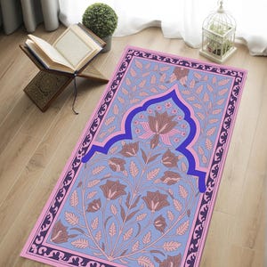 May include: A prayer rug with a floral design in shades of pink, blue, and purple. The rug features a central floral motif and an ornate border. The rug is rectangular and appears to be made of fabric.