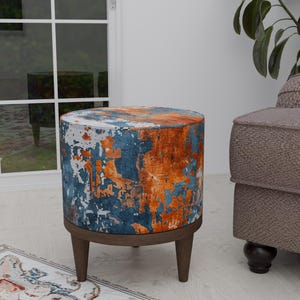 May include: A round, blue, orange, and white patterned ottoman with a wooden base and legs. The ottoman is sitting on a rug with a floral pattern.