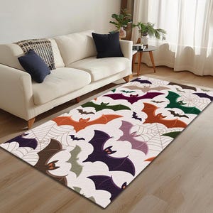 Puede incluir: Una alfombra rectangular con un patrón repetido de murciélagos y telarañas en varios colores, incluyendo naranja, morado, verde y marrón, sobre un fondo blanco. La alfombra está colocada sobre un suelo de madera en un salón.