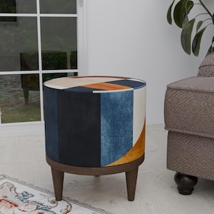 May include: A round, colorful ottoman with a geometric pattern in shades of blue, orange, yellow, and white. The ottoman has wooden legs and a dark brown base.