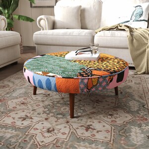 May include: A round ottoman featuring a patchwork design with various patterns including leopard print, monarch butterfly wings, and floral motifs in green, orange, and pink. The piece is supported by four tapered dark brown wooden legs.