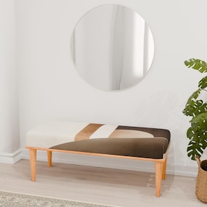 May include: A wooden bench with a white, brown, and beige geometric patterned cushion. The bench has four legs and is in a room with a round mirror and a potted plant.