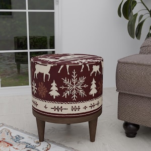 Peut inclure: Un pouf rond, rouge et blanc à motifs, avec des pieds en bois. Le pouf présente un motif de flocon de neige et des silhouettes de rennes.