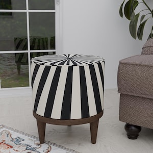 May include: A round ottoman with a black and white striped pattern. The ottoman has a wooden base and three legs. The design is reminiscent of a circus tent. The ottoman is placed near a window and a patterned rug.