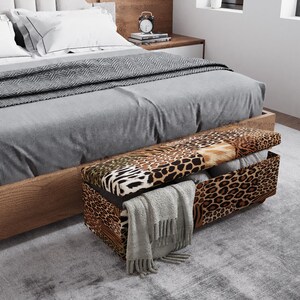 May include: A bedroom scene featuring a bed with gray bedding and a patterned throw. A storage bench with a leopard print design sits at the foot of the bed, with a gray blanket draped over the edge.