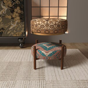 a modern living room with a rug, a colorful ottoman, and a large wall art piece.