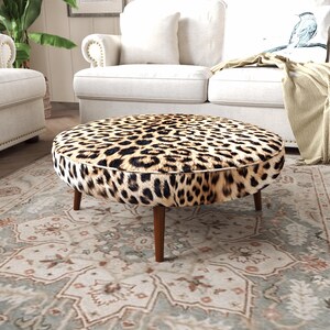 a living room with a leopard print ottoman in the center, surrounded by a white sofa and a patterned rug.