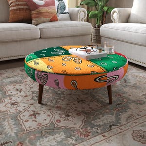 May include: A round ottoman featuring a multi-coloured patchwork design with green, orange, and pink sections, each decorated with a black and white paisley pattern. The piece is supported by four dark brown tapered wooden legs.
