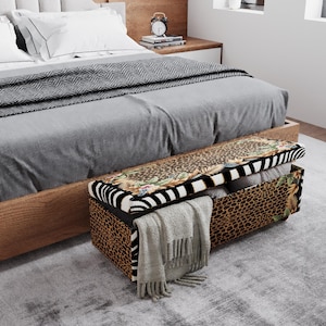 May include: A decorative storage bench with a hinged lid, featuring a zebra stripe and floral pattern on the top. The sides have a leopard print design. A gray blanket and other items are stored inside. The bench is placed at the foot of a bed.