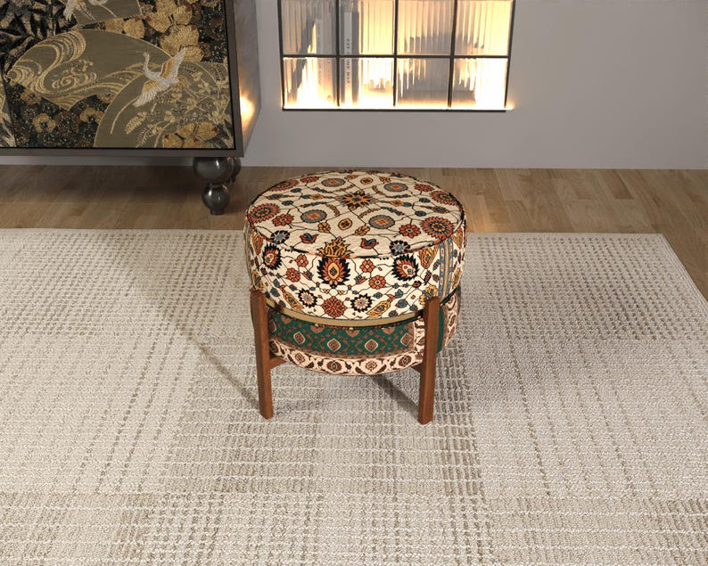 a round, colorful ottoman with a patterned design, placed on a beige rug in a room with a fireplace and a bookshelf.