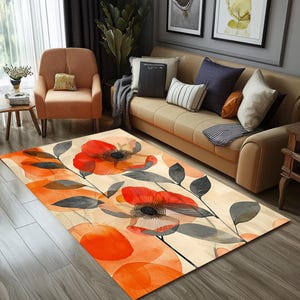 Op de afbeelding: Een beige vloerkleed met een bloemenpatroon met grote oranje bloemen en grijze bladeren. Het kleed heeft een aquareleffect en ligt op een houten vloer.