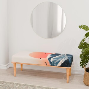 May include: A wooden bench with a white cushion featuring a colorful print of a sunset and waves. The bench is in a room with a round mirror and a potted plant.