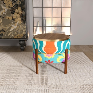 Peut inclure: Un pouf rond décoratif avec un dessus et une base en bois. Les côtés sont recouverts d'un tissu coloré avec un motif de vagues turquoise et blanches, orange et un motif floral. Le pouf mesure environ 46 cm de diamètre et 41 cm de haut.