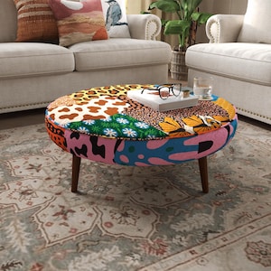 Puede incluir: Un otomán redondo con un diseño de patchwork que incluye varios patrones como estampado de leopardo, manchas de vaca, motivos florales y formas abstractas en colores vibrantes. La pieza se apoya sobre cuatro patas de madera marrón oscuro.