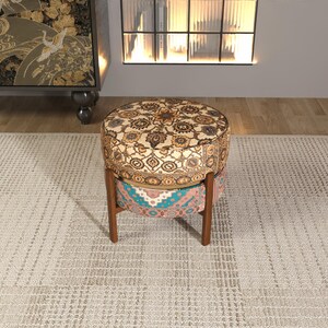 a decorative ottoman with a patterned design, placed on a rug in a room with a bookshelf and a window.