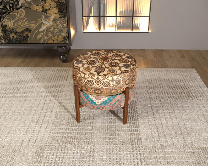 a decorative ottoman with a patterned design, placed on a rug in a room with a bookshelf and a window.