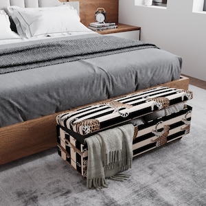 May include: A storage bench with a black and white striped pattern and leopard print accents. The bench is open, revealing pillows and a folded blanket. The bench is placed at the foot of a bed with gray bedding.