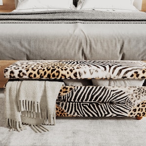 Könnte beinhalten: Ein rechteckiger Aufbewahrungshocker mit einem gemischten Tiermuster aus schwarz-weißen Zebrastreifen und braun-schwarzen Leopardenflecken. Der Deckel ist leicht geöffnet und gibt den Blick auf den Stauraum und eine beige Decke frei.