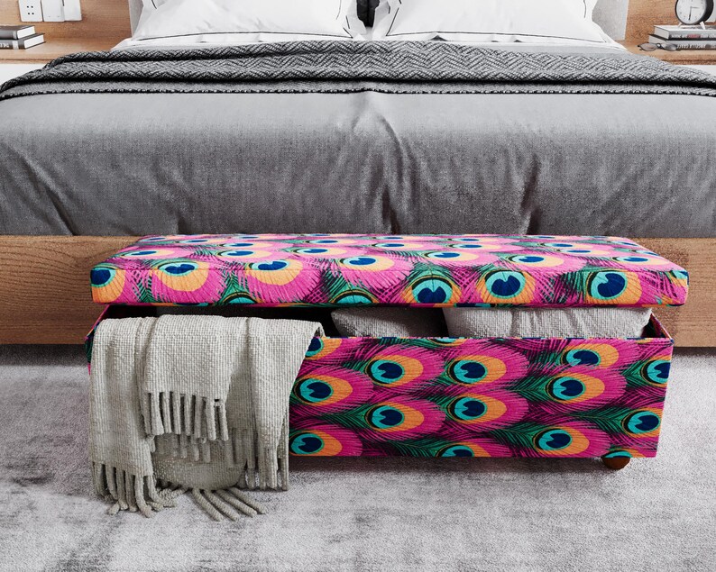 A colorful storage bench with a patterned design sits on a gray carpeted floor in front of a bed.
