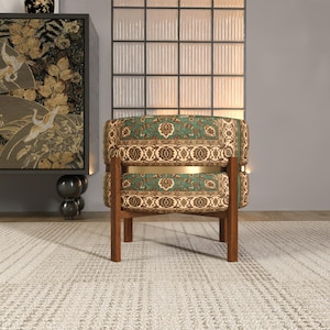 a chair with a green and gold patterned cushion, placed on a white rug in a room with a large window and a decorative cabinet.