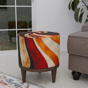 Peut inclure: Un ottoman rond en bois avec un motif abstrait coloré dans des tons d'orange, de rouge, de noir et de blanc. L'ottoman a quatre pieds en bois.