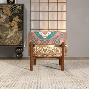 a colorful, patterned chair with a wooden frame, placed on a white rug in a room with a large window and a decorative wall.
