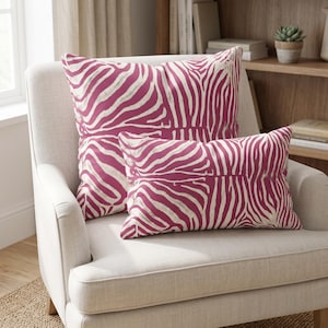 May include: Two throw cushions featuring a vibrant magenta and white zebra stripe pattern. One cushion is square-shaped and positioned behind a smaller, rectangular-shaped cushion. Both cushions display the same bold animal print design throughout.