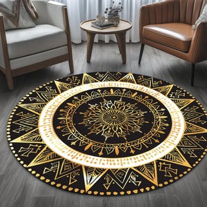 Puede incluir: Una alfombra redonda negra con un diseño geométrico dorado y blanco. La alfombra presenta un patrón central tipo mandala, una banda blanca y un borde de triángulos y formas doradas. Está colocada sobre un suelo de madera.