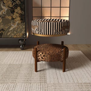a modern living room with a leopard print ottoman and a striped ottoman, both placed on a white rug. The room has a minimalist design with a large window and a black and white patterned wall hanging.