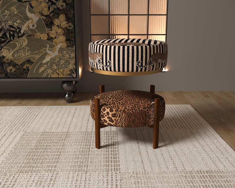 a modern living room with a leopard print ottoman and a striped ottoman, both placed on a white rug. The room has a minimalist design with a large window and a black and white patterned wall hanging.
