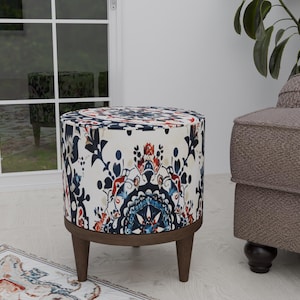 May include: A round, white ottoman with a blue and red floral pattern. The ottoman has a wooden base and four legs.