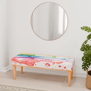 May include: A wooden bench with a colorful abstract design on the seat. The design features a rainbow of colors, including pink, orange, yellow, green, blue, and purple. The bench has a white background and is accented with wooden legs.