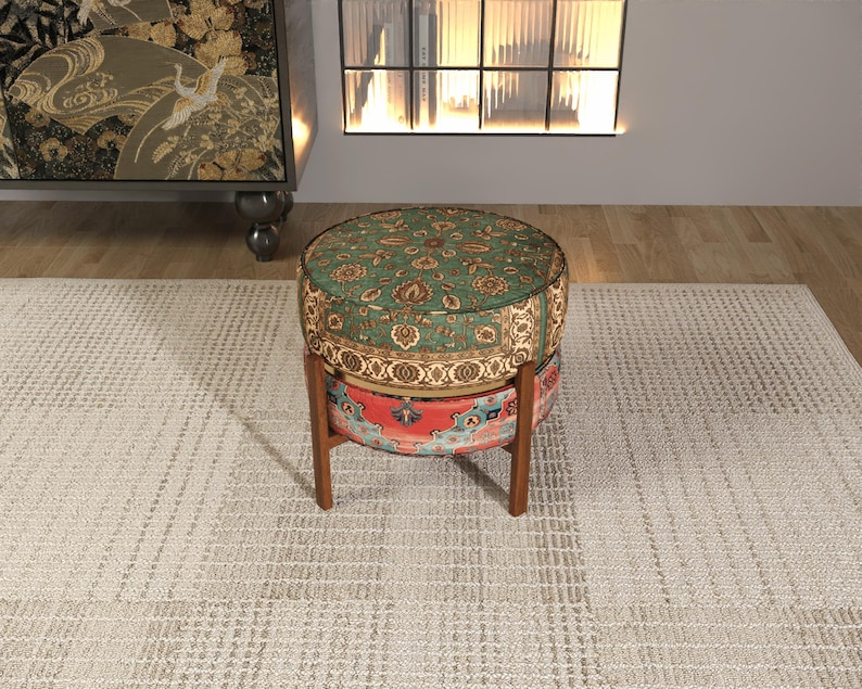 a round, colorful ottoman with a patterned design, placed on a white rug in a room with a bookshelf and a window.