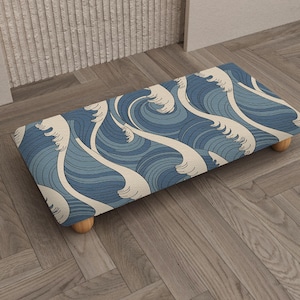 May include: A rectangular footstool with a blue and white wave pattern. The stool has a wooden frame and four rounded wooden legs. The wave design features shades of blue and white, creating a nautical theme.