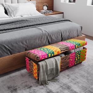 Könnte beinhalten: Bunte Aufbewahrungsbank mit gemustertem Design vor einem Bett. Die Bank hat eine Mischung aus leuchtenden Farben und Mustern, darunter Pink, Grün, Gelb und Zebrastreifen. Eine graue Decke und andere Gegenstände werden darin aufbewahrt.