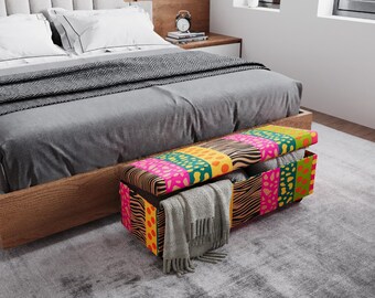 May include: A colorful storage bench with a patterned design sits at the foot of a bed. The bench features a mix of vibrant colors and patterns, including pink, green, yellow, and zebra print. A gray blanket and other items are stored inside.