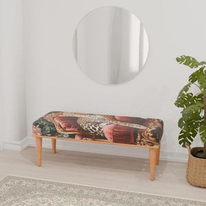 May include: A wooden bench with a leopard print and floral patterned cushion. The bench has a natural wood finish and is sitting on a patterned rug in front of a white wall.