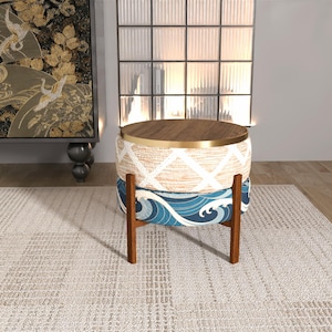 May include: A round accent table with a wooden top and a gold-colored metal band. The table has a woven beige and white patterned middle section and a blue wave-patterned base. It stands on a dark brown wooden frame.