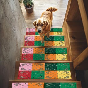 Può includere: Un cane Golden Retriever scende una scala di legno adornata con gradini colorati. Ogni gradino presenta un design patchwork con motivi paisley in rosso, rosa, verde, arancione e giallo. La scala fa parte di un interno.