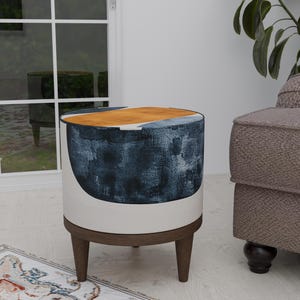 Könnte beinhalten: Ein runder, weißer Hocker mit einem abstrakten Design in Blau und Gelb. Der Hocker hat Holzbeine und steht auf einem Teppich.