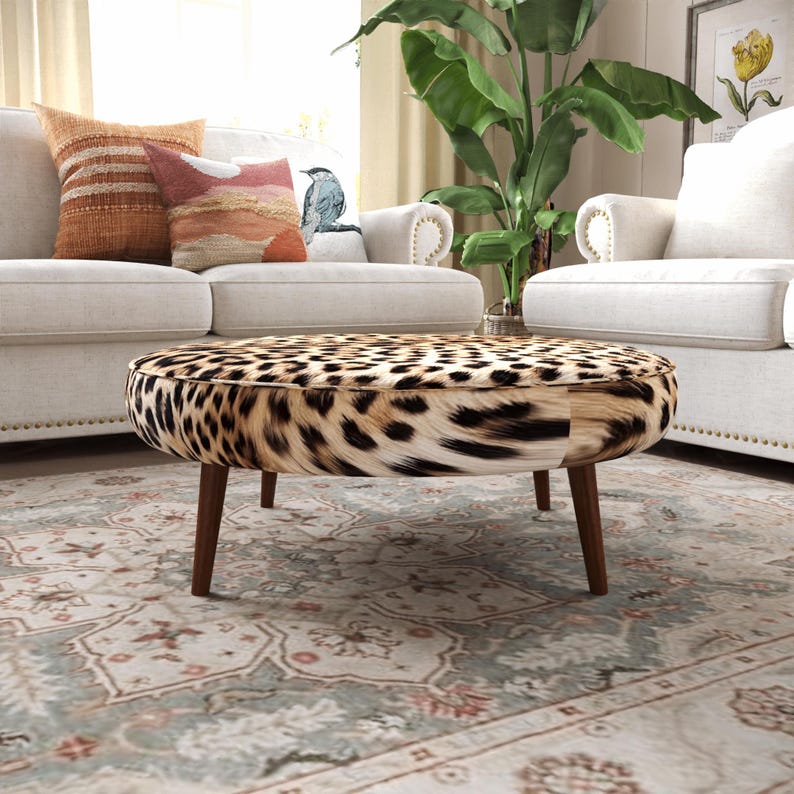 a living room with a leopard print ottoman in the center, surrounded by white furniture and a large potted plant.
