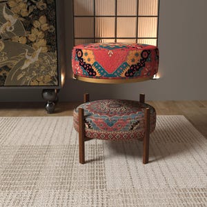 a modern living room with a rug, a colorful ottoman, and a large painting on the wall.