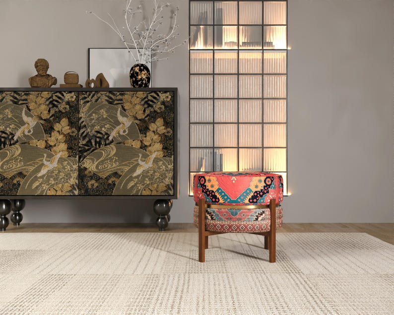 a modern living room with a vibrant red and blue patterned chair, a black and gold cabinet with a floral design, and a glass-paneled wall with a white vase and branches.