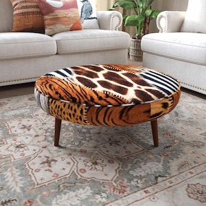 Könnte beinhalten: Ein runder Hocker mit einem Patchwork-Design aus verschiedenen Tiermustern, darunter Giraffenflecken, Zebrastreifen und Tigerstreifen. Das Möbelstück steht auf vier konisch zulaufenden Holzbeinen und weist sichtbare weiße Nähte auf.