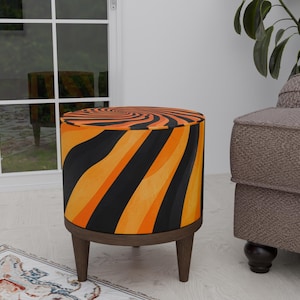 May include: Orange and black striped ottoman with wooden legs. The ottoman has a swirling pattern.