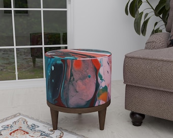 Puede incluir: Un puf redondo y colorido con un patrón abstracto de espiral en rosa, azul, verde y naranja. El puf tiene una base de madera oscura y tres patas.