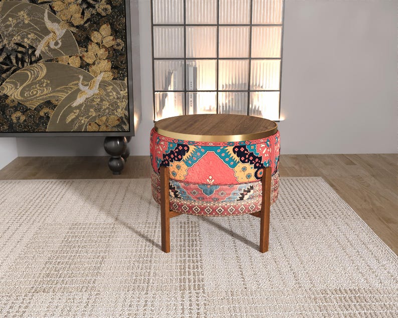 a colorful, patterned ottoman or stool with a wooden top, placed on a white rug in a room with a large window and a painting on the wall.