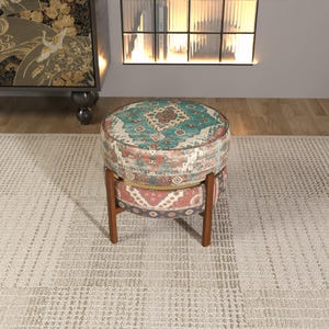 a round, colorful ottoman with a patterned design, placed on a beige rug in a room with a fireplace and a bookshelf.