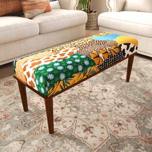 Peut inclure: Un banc rectangulaire rembourré présentant un motif patchwork vibrant avec divers imprimés incluant des taches de léopard, des taches de vache, des vagues bleues, un nid d'abeille jaune, des papillons orange et un motif floral vert sur quatre pieds en bois.