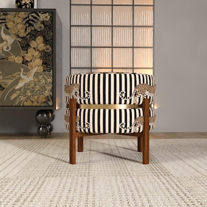 a stylish chair with a black and white striped pattern, placed on a white rug in a room with a large window and a decorative cabinet.